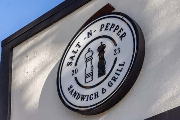 Salt N Pepper Sandwich & Grill restaurant logo sign mounted on a modern white storefront exterior, featuring a salt and pepper shaker emblem and bold circular branding.