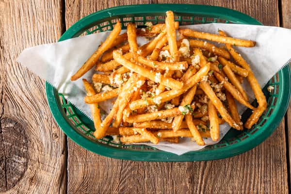 Basket of crispy garlic Parmesan French fries topped with herbs and grated cheese served in a green basket.