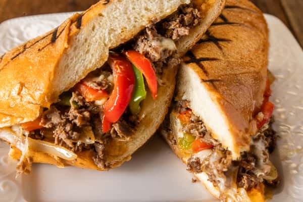 Close-up of a Philly cheesesteak sandwich with seasoned steak, melted cheese, sautéed onions, and red and green bell peppers on grilled bread.