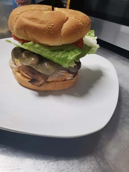 Grilled chicken sandwich with melted cheese, mushrooms, lettuce, and tomato on a toasted bun, served on a white plate.