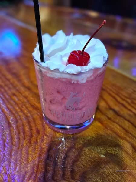Creamy cherry milkshake or cocktail topped with whipped cream and a maraschino cherry, served in a Pendleton Whisky glass.