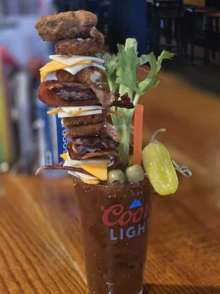 Image Alt Text Generator said: This is an extravagant Bloody Mary served in a Coors Light glass, garnished with an impressive skewer tower