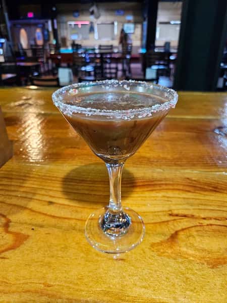 Chocolate martini with a sugared rim served in a classic martini glass on a wooden bar counter.