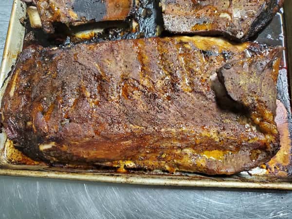 Juicy, slow-smoked beef brisket resting on a baking tray, glistening with rendered fat and a dark seasoned bark.