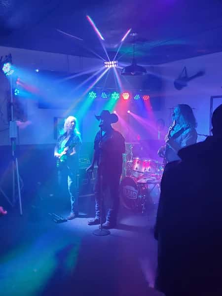 Live band performing under vibrant stage lights with a cowboy-hat-wearing lead singer and guitarists on either side.