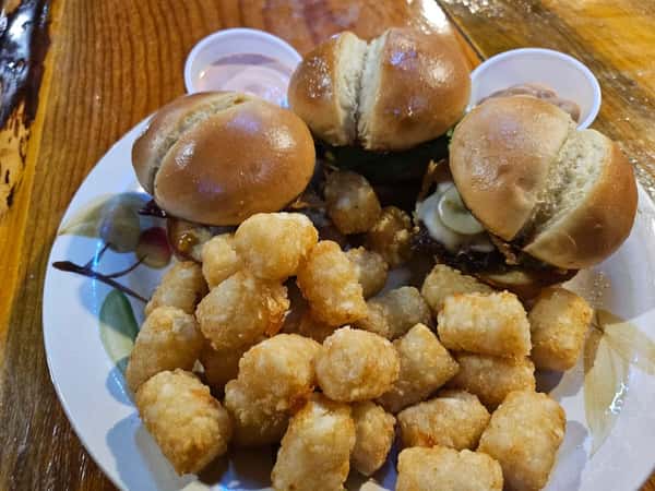 Mini cheeseburger sliders served with crispy tater tots and dipping sauces on a decorative plate.