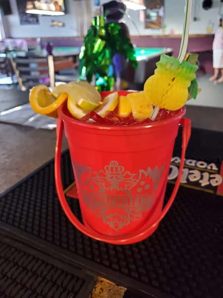 Bright red Smirnoff bucket cocktail garnished with lemon, lime, orange slices, and a decorative pineapple stirrer.