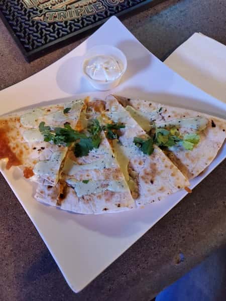 Cheese quesadilla slices topped with cilantro and drizzle, served with a side of sour cream on a white square plate.