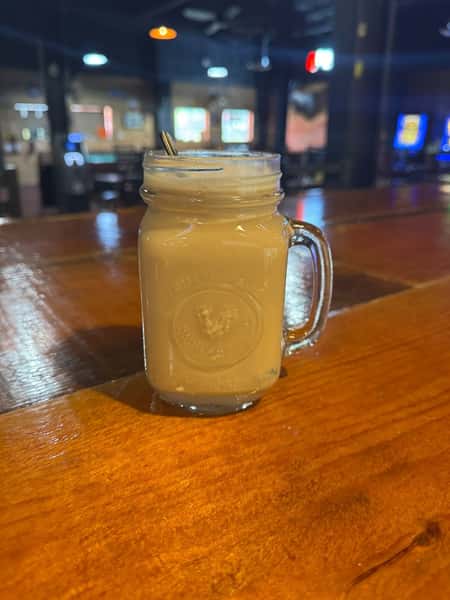Creamy iced coffee or cocktail served in a mason jar with a handle, topped with foam and a mini gold cocktail spoon.
