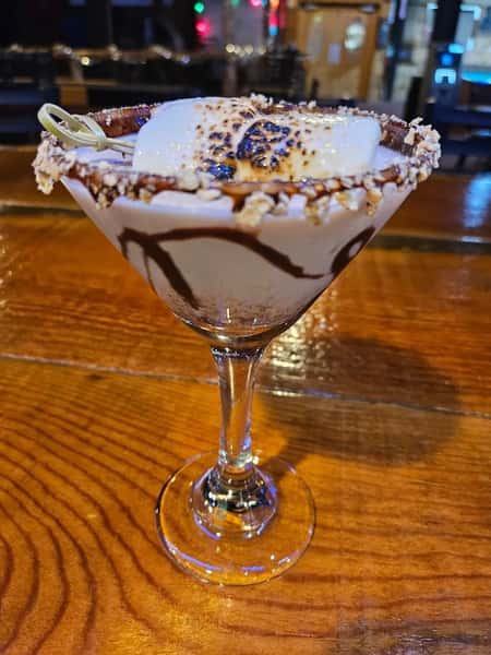 Dessert cocktail with a toasted marshmallow, chocolate drizzle, and crushed graham cracker rim served in a martini glass.