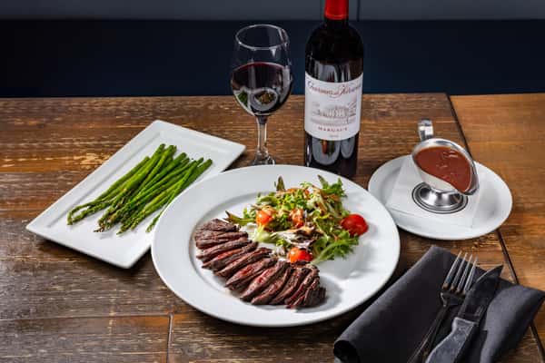 hanger steak with vegetables, and a glass and bottle of red wine