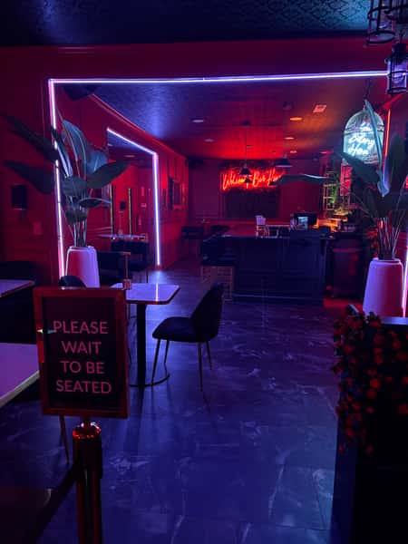Moody blue-lit lounge with marble-top tables, black chairs, a neon square wall display.