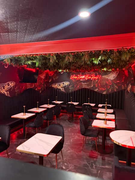 Interior of a restaurant with red walls, featuring a TV, vintage-style portraits, a flower-decorated counter, and elegant black chairs with gold accents.
