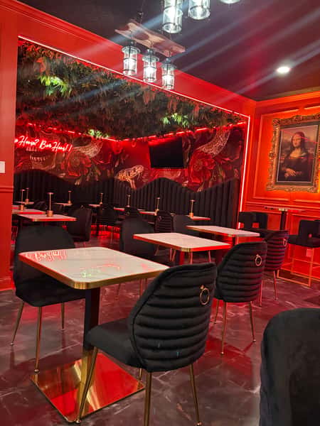 Interior of a restaurant with red walls, featuring a TV, vintage-style portraits, a flower-decorated counter, and elegant black chairs with gold accents.