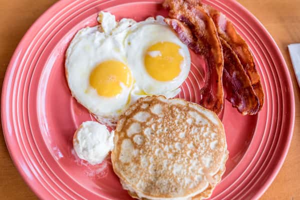 breakfast plate with pancakes, bacon and eggs