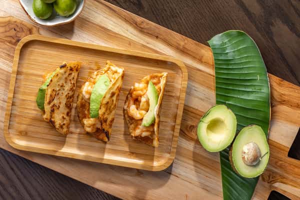 three crispy shrimp tacos on a wooden serving board, garnished with avocado slices and fresh toppings