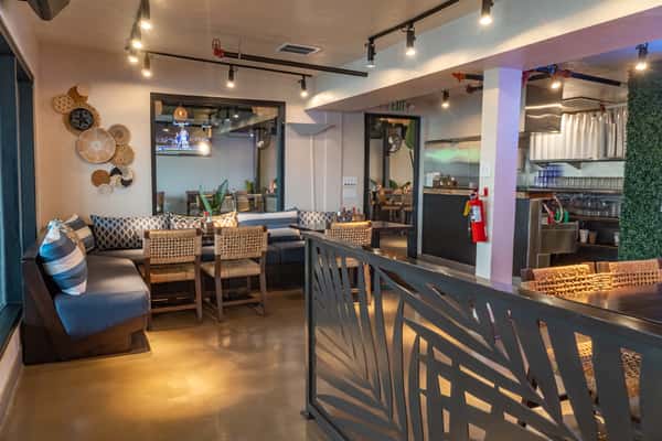 Stylish restaurant interior at dusk with decorative metal partition, warm track lighting, woven furniture, and an open layout