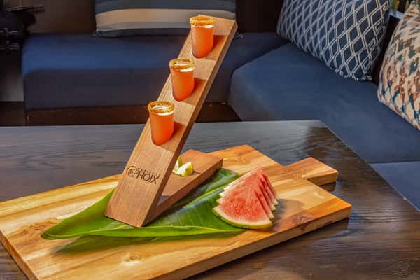 Branded wooden shot flight board holding four mini cocktail shots, served with watermelon slices on a banana leaf