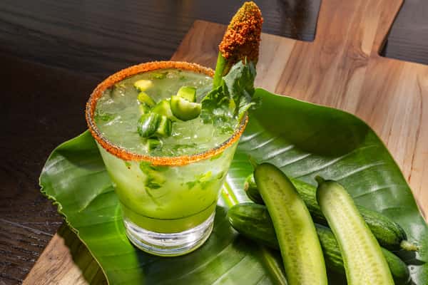 Cucumber jalapeño margarita with a chili-salt rim, garnished with fresh jalapeño and cucumber slices on a wooden surface