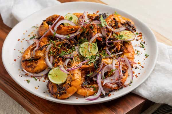 "Camarones Cucarachas" Sautéed spicy shrimp topped with sliced red onion, lime, fresh herbs, and chili flakes on a white plate