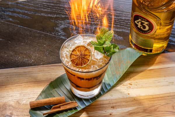"Carajillo" Amber-colored Licor 43 cocktail with a mint garnish and cinnamon sticks