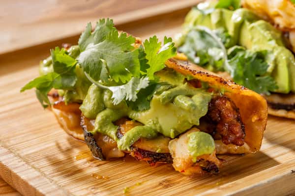 "Tacos Pulpo Zarandeado" Crispy octopus tacos topped with a generous layer of guacamole and fresh cilantro on a wooden surface