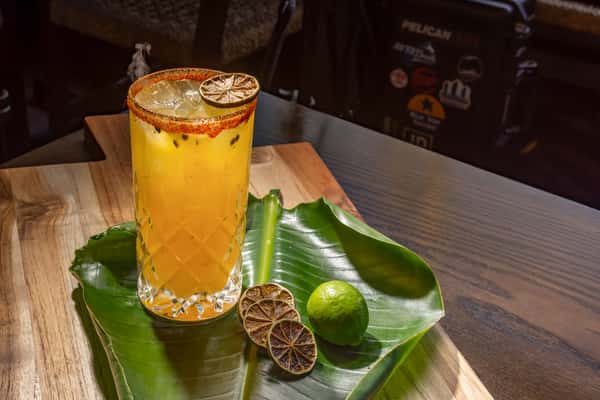 Yellow maracuya margarita with Tajín rim on top of a banana leaf on a wooden board