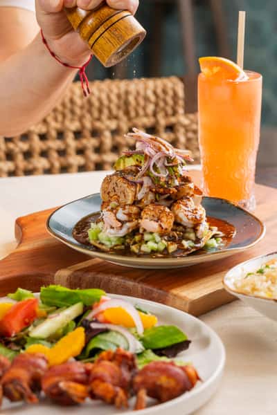 Chef special tostada with shrimp, house salad and drink in background