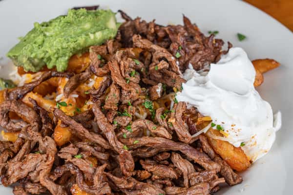 Seasoned beef fajita fries topped with grilled meat, guacamole, and sour cream.