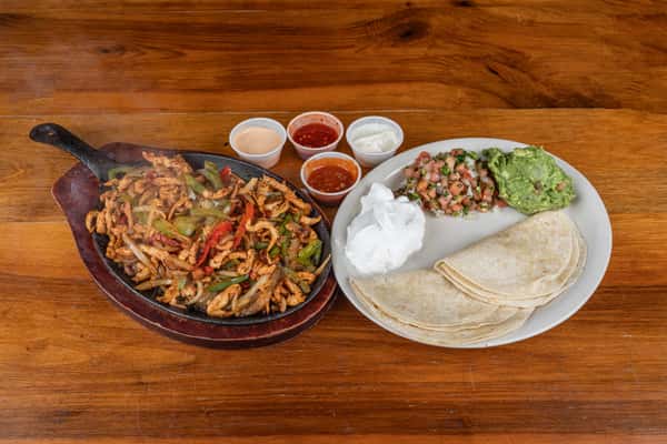 Sizzling chicken fajita skillet with warm tortillas, guacamole, pico de gallo, and sour cream.