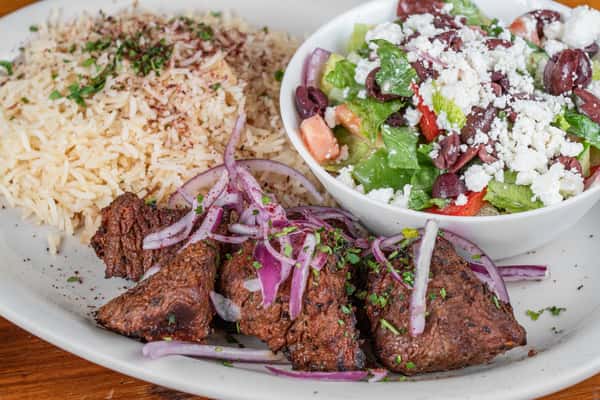 Grilled beef kabob plate with seasoned rice, fresh salad, vegetables, and sauces.