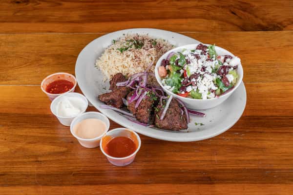 Grilled beef kabob plate with seasoned rice, fresh salad, vegetables, and sauces.
