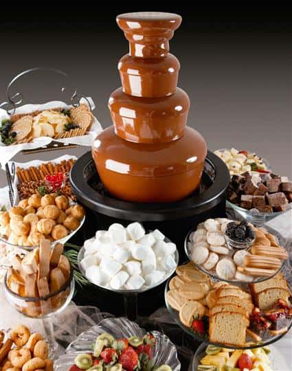 A chocolate fountain surrounded with a variety of catering dishes