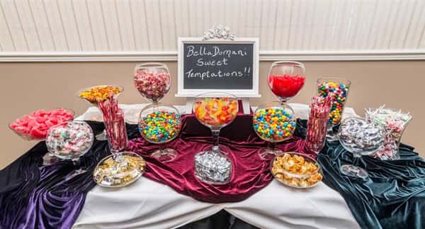 A buffet with a variety of sweets and a blackboard with the text "Bella Domani Sweet Temptations!!"