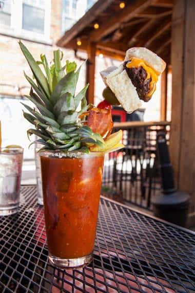 bloody mary with the top of a pineapple as a garnish also with a cheeseburger, bacon, olives and celery on a stick