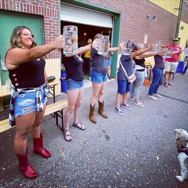 Group of participants lined up outside Old 121 Brewhouse, holding large empty beer steins straight out in a fun endurance competition.