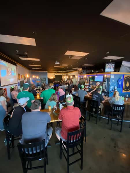 Large crowd gathered around tables and the bar inside Old 121 Brewhouse for a social event.