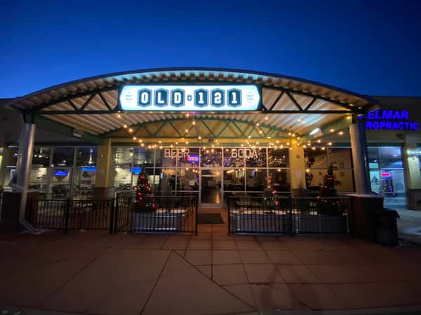 Illuminated Old 121 Brewhouse storefront with festive string lights and decorated Christmas trees on the patio, creating a welcoming evening atmosphere.