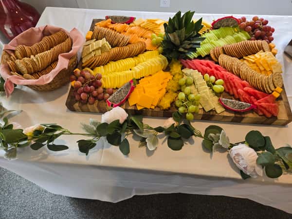 A colorful catering platter featuring an array of cheeses, fruits, and crackers, beautifully arranged with a pineapple centerpiece and garnished with greenery along the table.