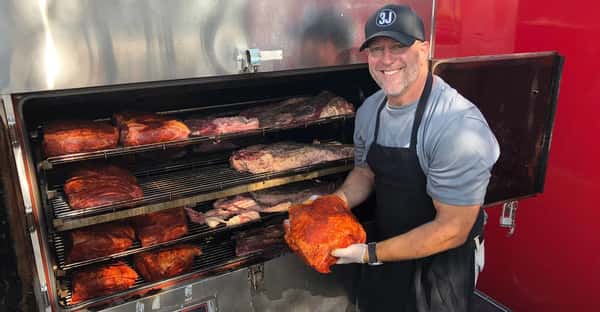 Owner holding a piece of meat over a grill