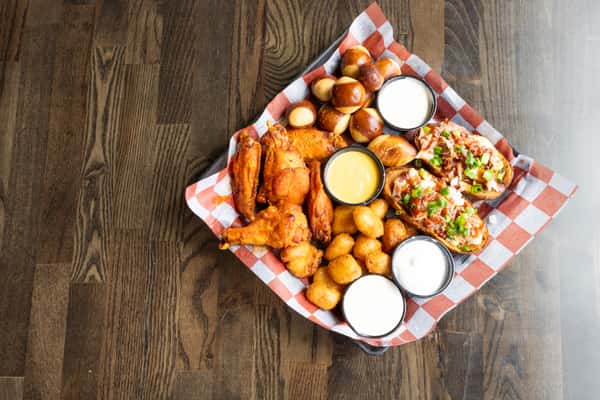 Overhead view of a bar appetizer sampler with wings, pretzel bites, potato skins, tater tots, and dipping sauces