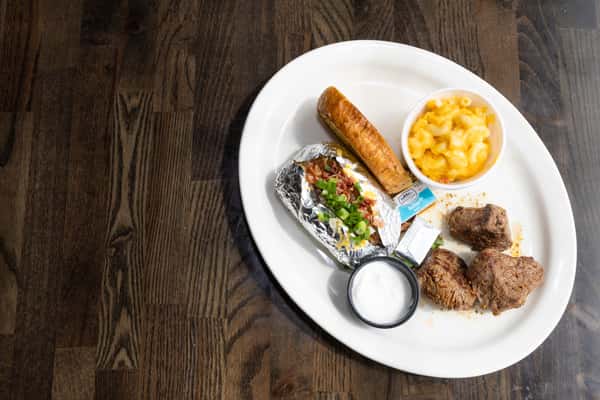 Steakhouse plate with grilled steak tips, loaded baked potato, mac and cheese, and garlic bread on a white plate