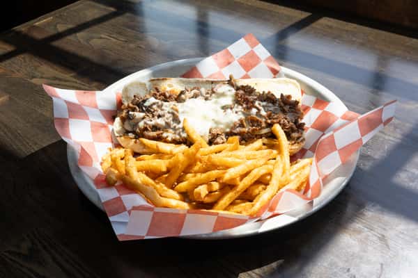 Philly cheesesteak sandwich with melted cheese and grilled onions served with crispy French fries on a checkered tray