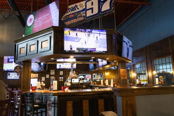 Sports bar interior with central bar seating, multiple TVs showing games, and a warm casual dining atmosphere