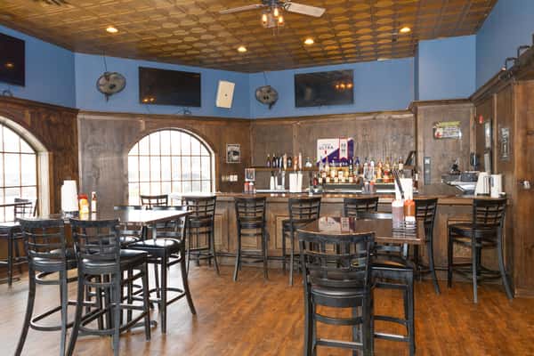 casual bar dining area with wood floors, high top tables, and full bar with TVs in a relaxed brewpub setting