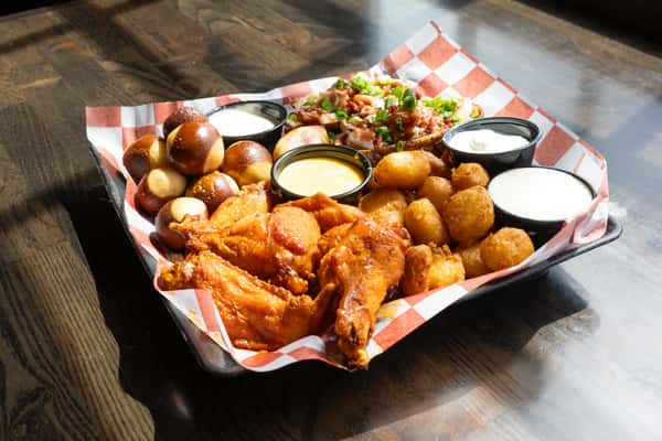 Loaded sampler platter with buffalo wings, pretzel bites, tater tots, potato skins, and dipping sauces on checkered paper
