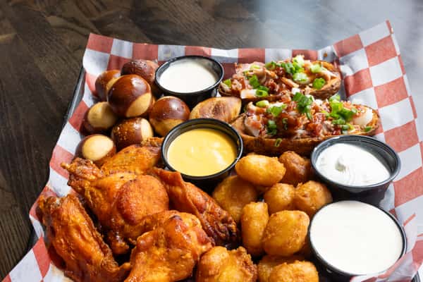 Crispy buffalo wings platter with pretzel bites, tater tots, loaded potato skins, and assorted dipping sauces on a checkered tray