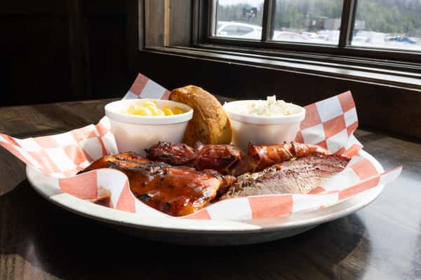 BBQ plate with glazed ribs, smoked sausage, sliced brisket, mac and cheese, coleslaw, and garlic toast