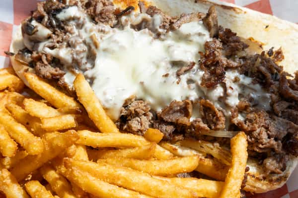 Philly cheesesteak sandwich with melted provolone, grilled onions, and crispy French fries on a deli-style tray