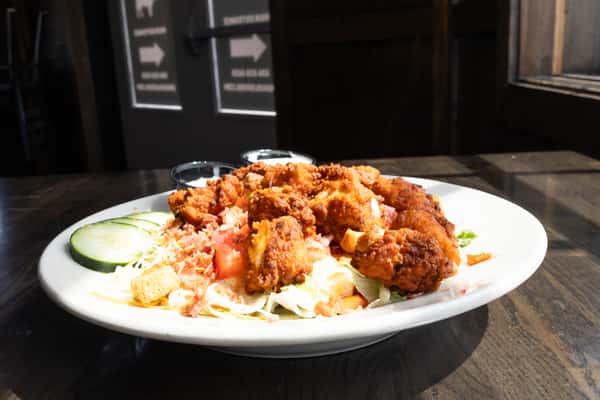 Buffalo chicken salad with crispy fried chicken, bacon, tomatoes, cucumbers, shredded cheese, and ranch dressing on a white plate